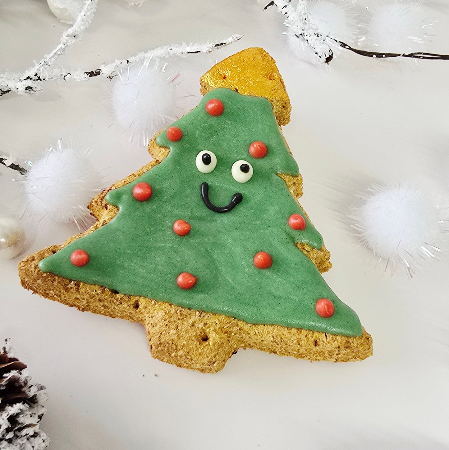 Decorative Christmas tree cookie with a face on a white background with pinecones and branches.