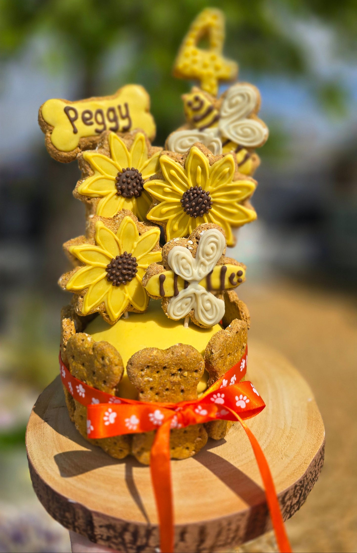 Decorative cookie with flowers and a bee, attached to a wooden spool with a ribbon.