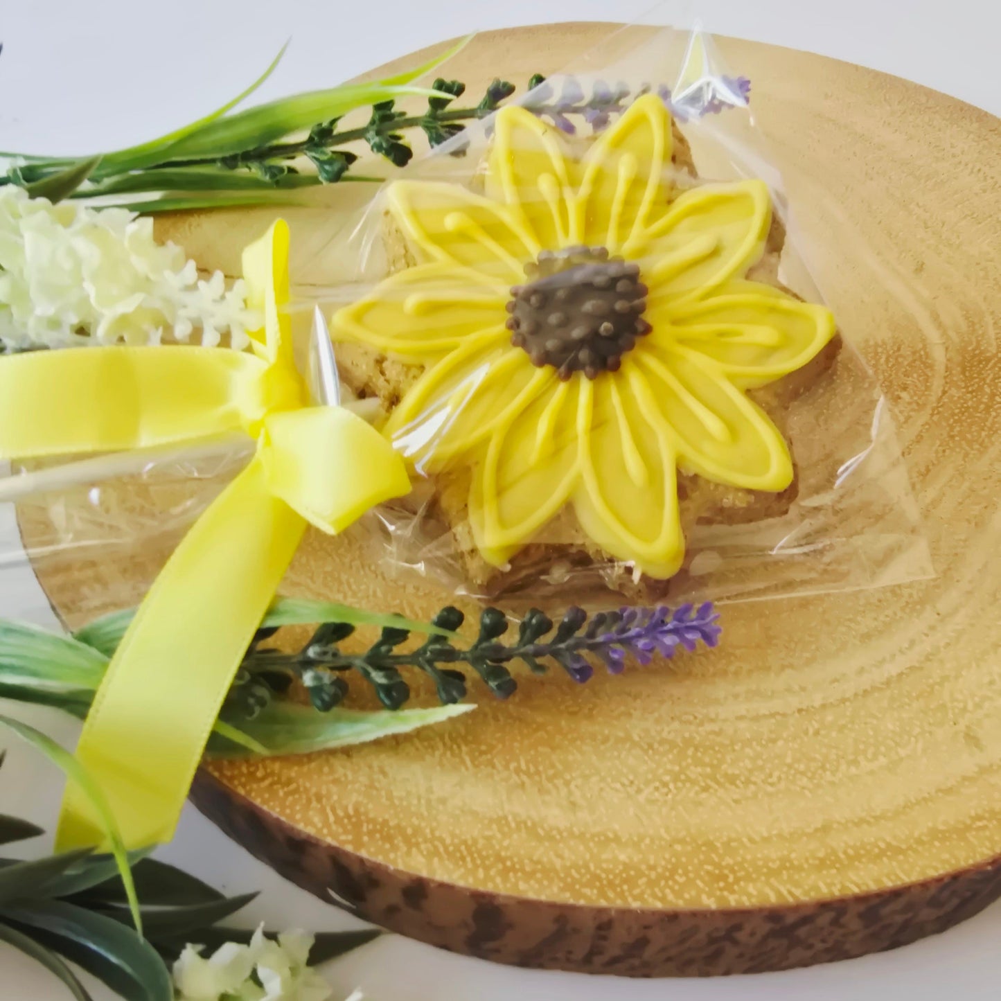 Decorative arrangement with a sunflower, lavender, and yellow ribbon on a wooden board.