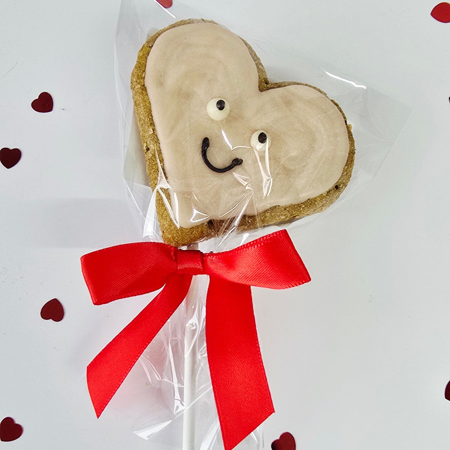 Heart-shaped cookie with a smiley face and red ribbon on a white background with small red hearts.