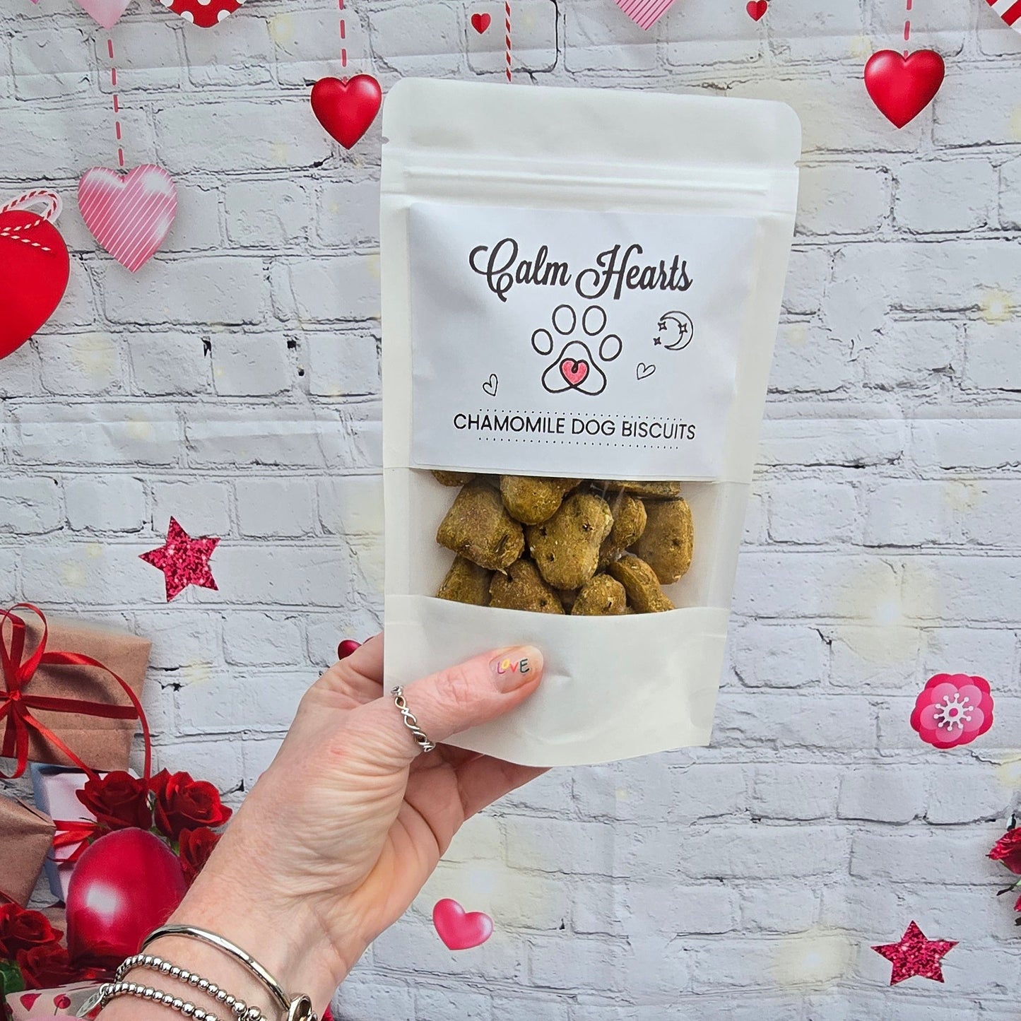 Hand holding a small bag of pet treats with a heart-themed background