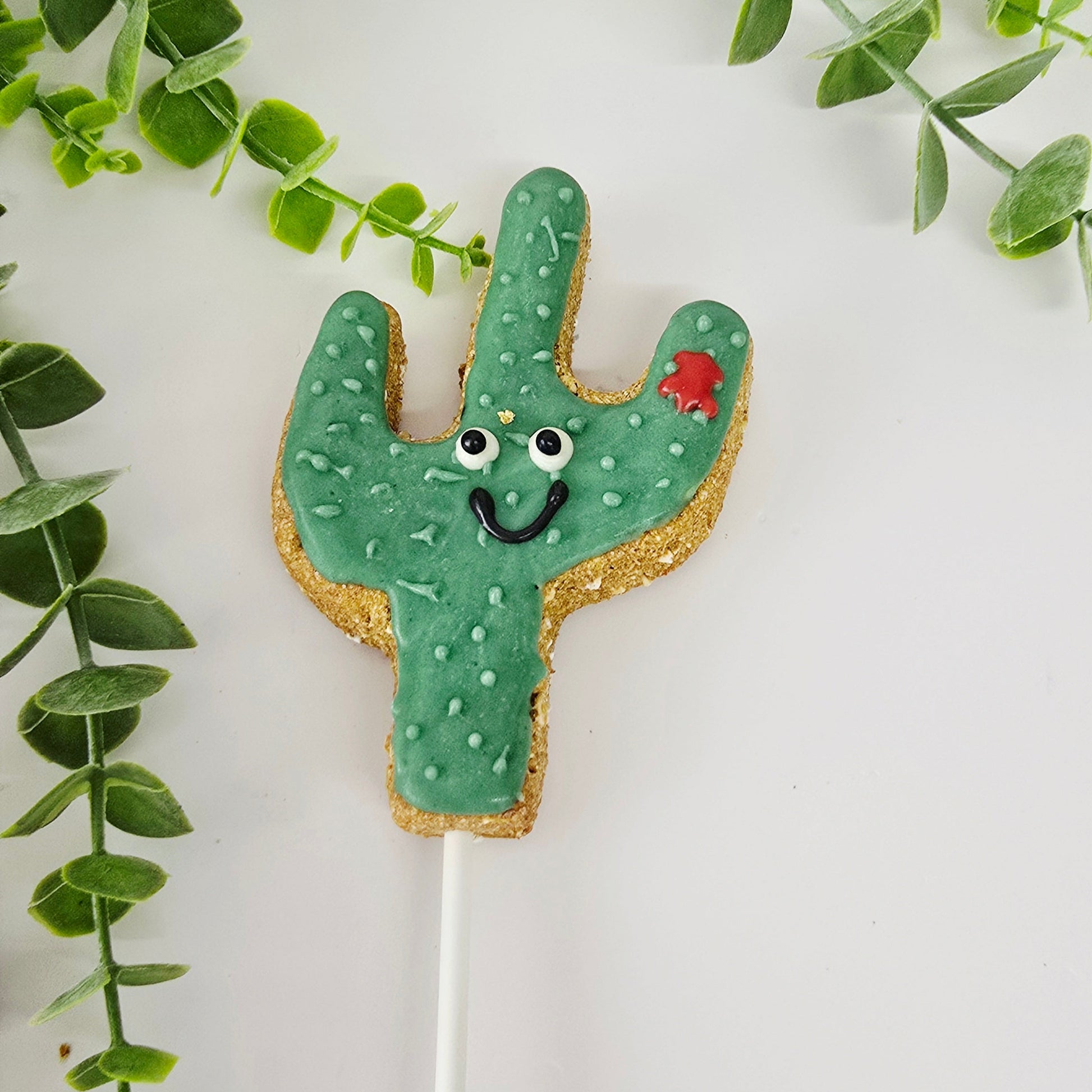 Cactus-shaped cookie on a stick with green leaves in the background