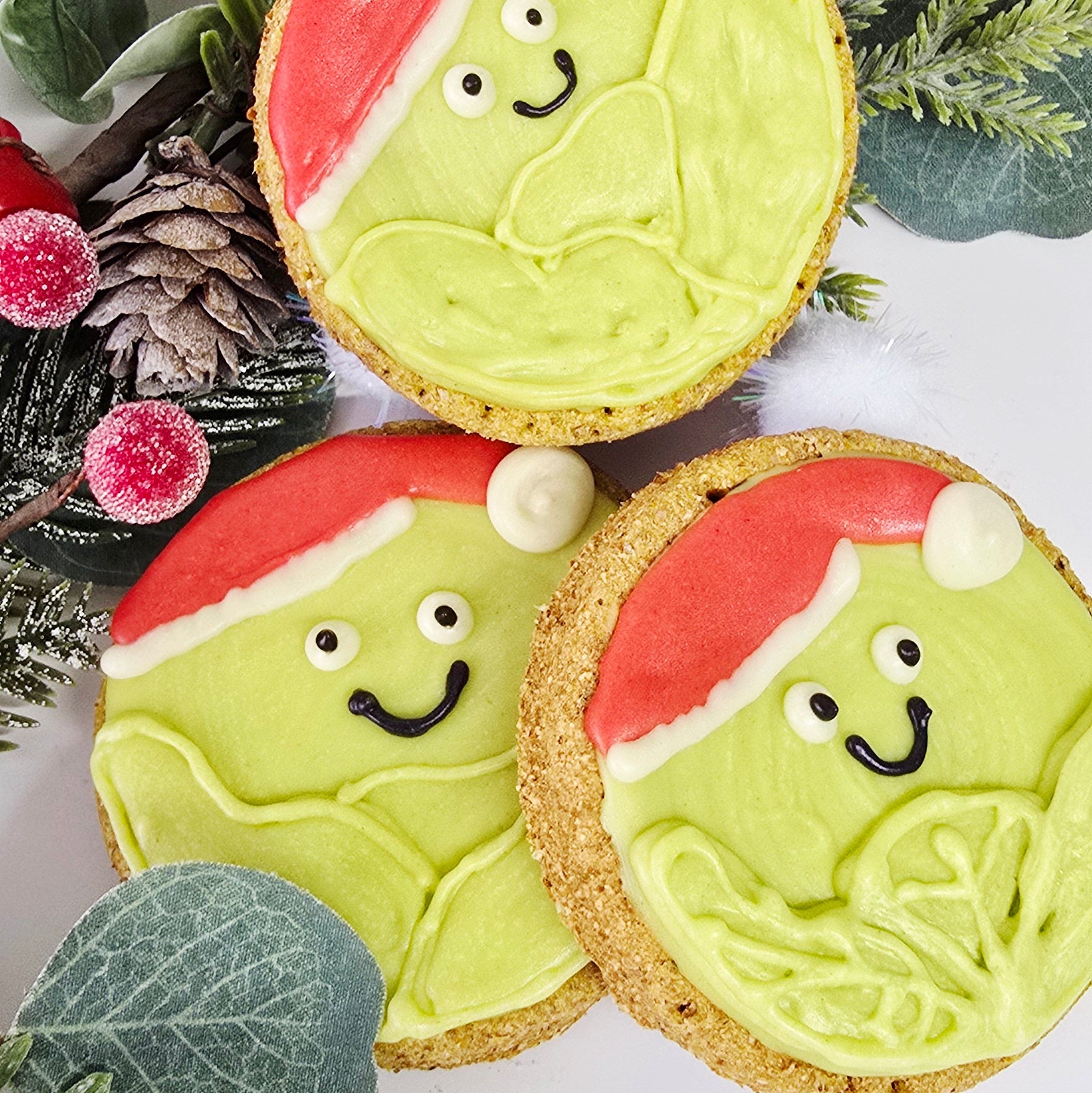 Decorative cookies with face designs on a white background with greenery