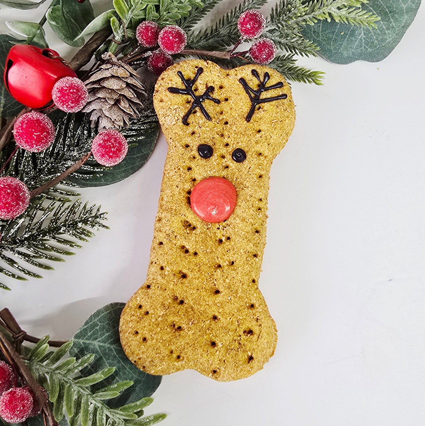Decorative dog bone treat with berries and greenery on a white background