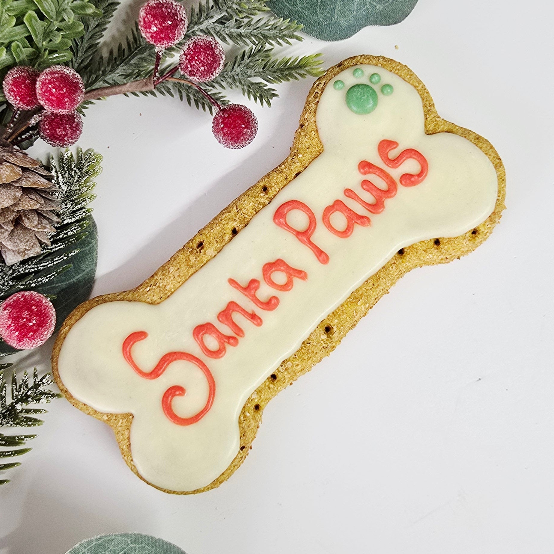 Dog bone-shaped cookie with 'Santa Paws' text on a white background with greenery.