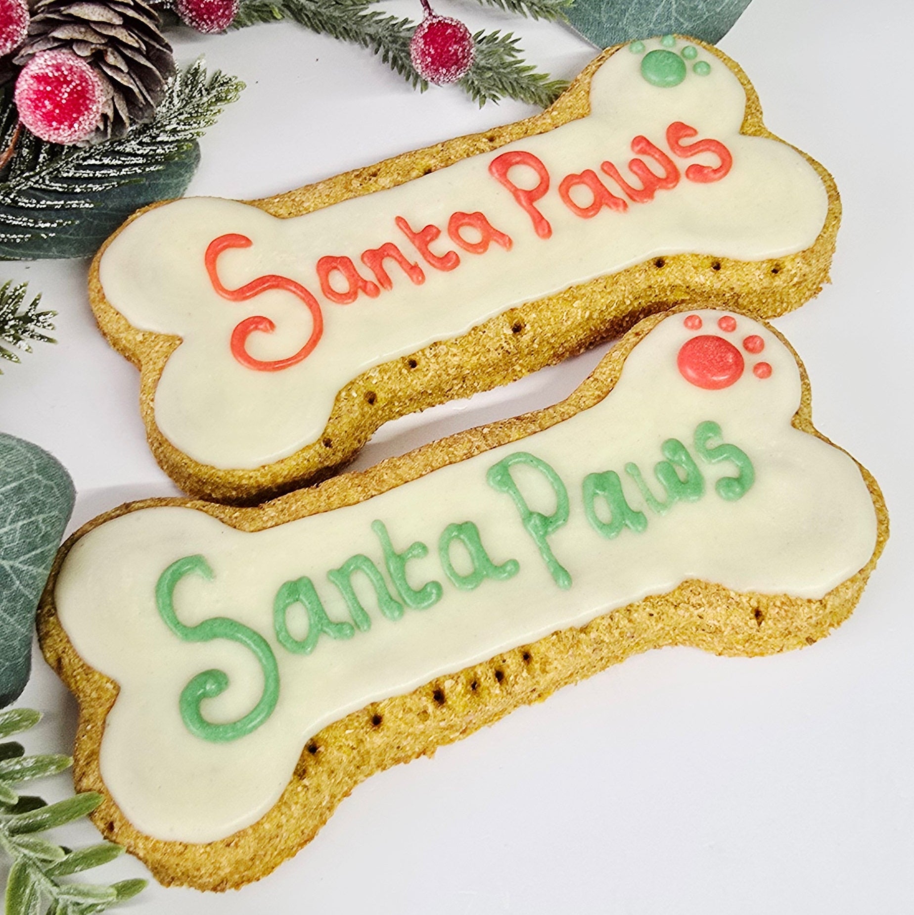 Two bone-shaped cookies with 'Santa Paws' text on a white background with Christmas decorations.