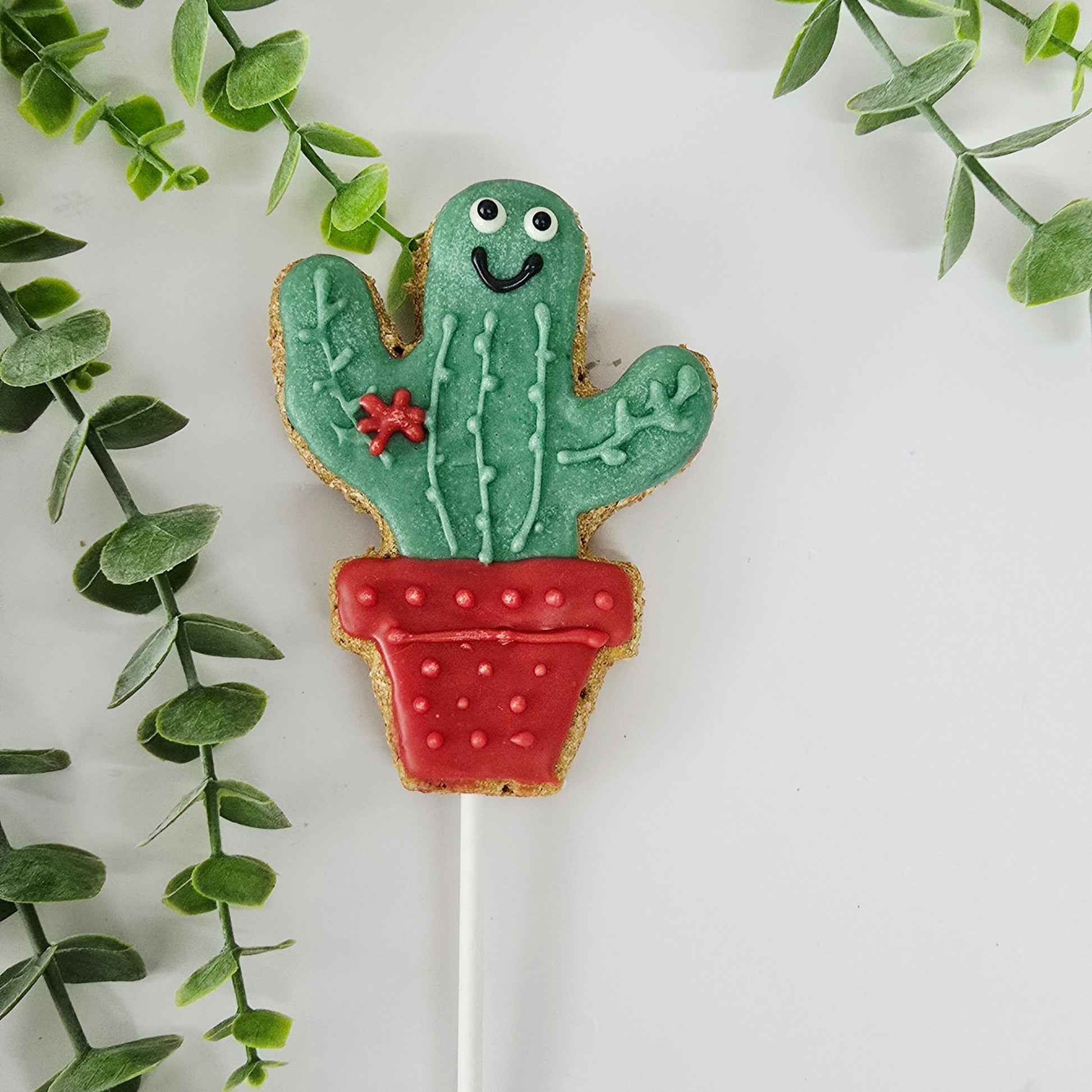 Cactus-shaped cookie on a stick with green leaves in the background