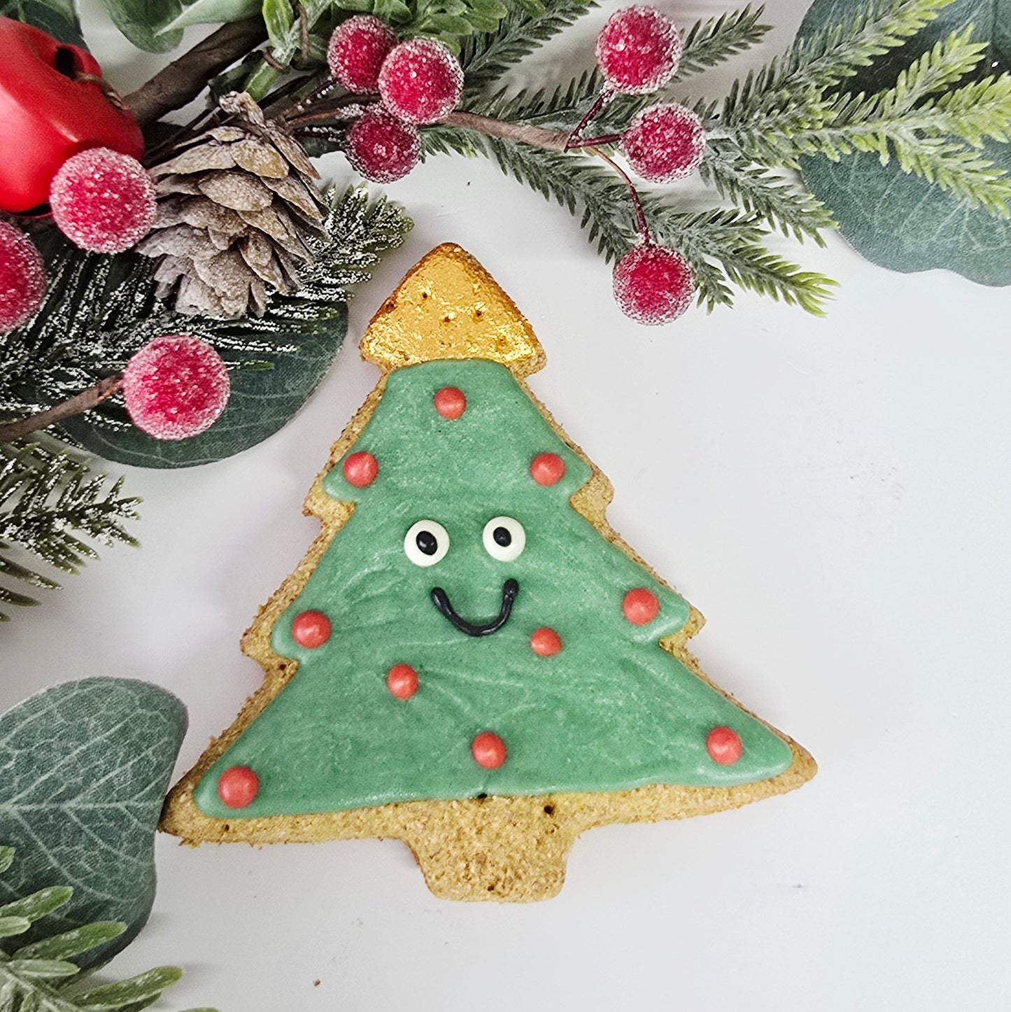 Christmas-themed cookie with tree design surrounded by greenery and berries on a white background