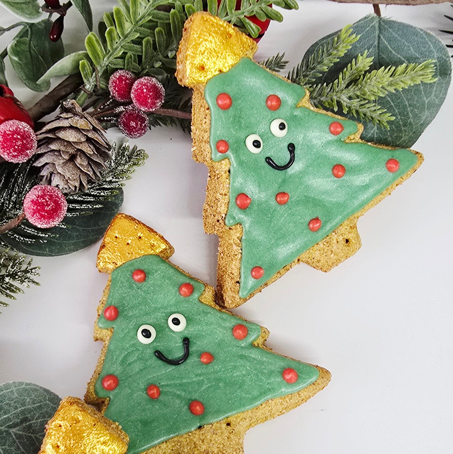 Decorative Christmas tree cookies with gold accents on a white background with greenery.