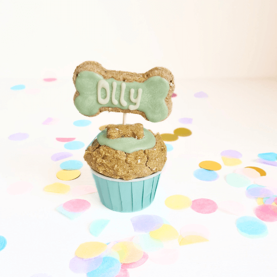 doggie cupcake handmade with a bone shapred treat on top iced with dog friendly caron and personalised  with teh dogs name Oliie ,pictured with a party confetto background