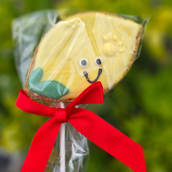 lemon shaped Cookie on a stick with a face and red ribbon against a blurred green background