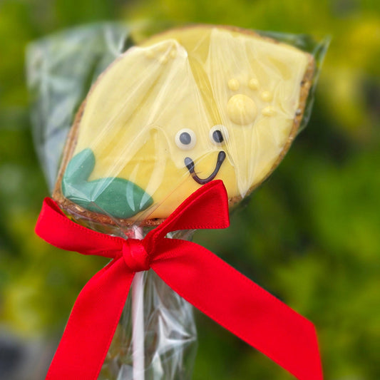 lemon shaped Cookie on a stick with a face and red ribbon against a blurred green background