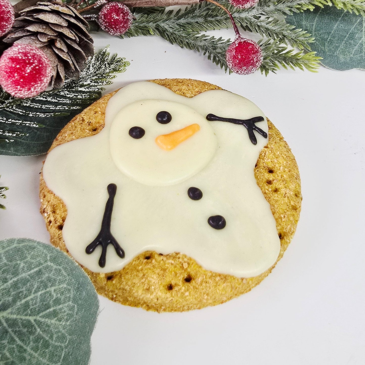 Decorative cookie shaped like a snowman with greenery and berries on a white background