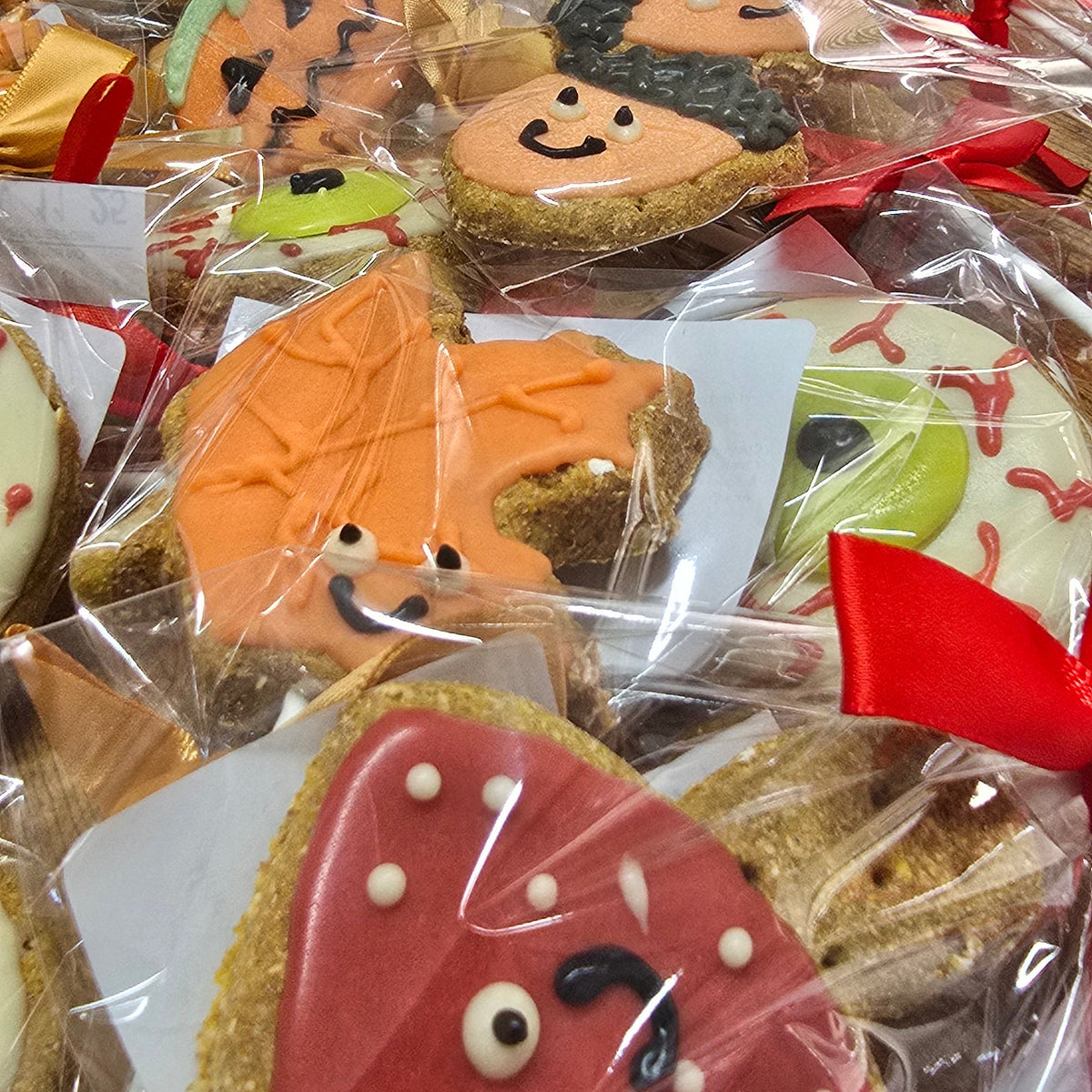 Decorated sugar cookies wrapped in clear cellophane bags with gold and red ribbons, displayed on a table with cardboard boxes in the background.