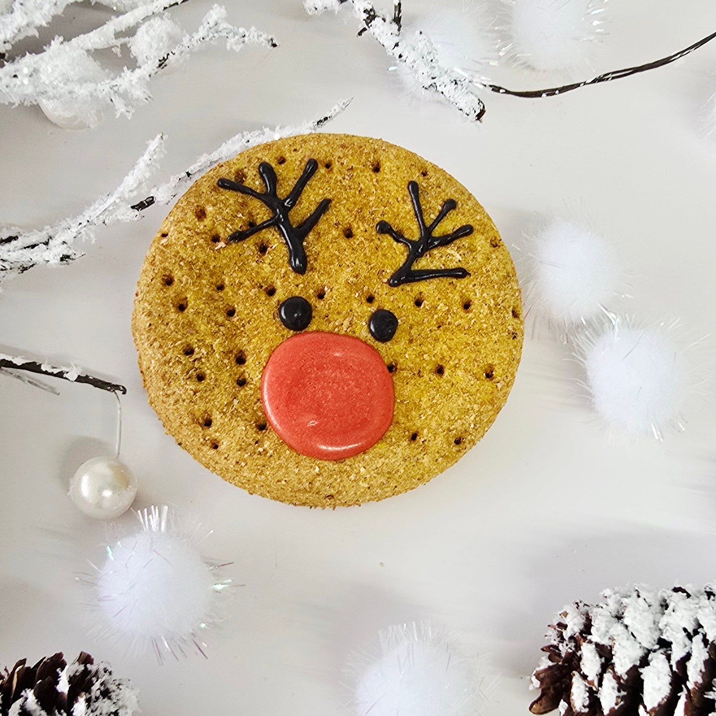 Cookie with a reindeer face surrounded by decorative elements on a light background