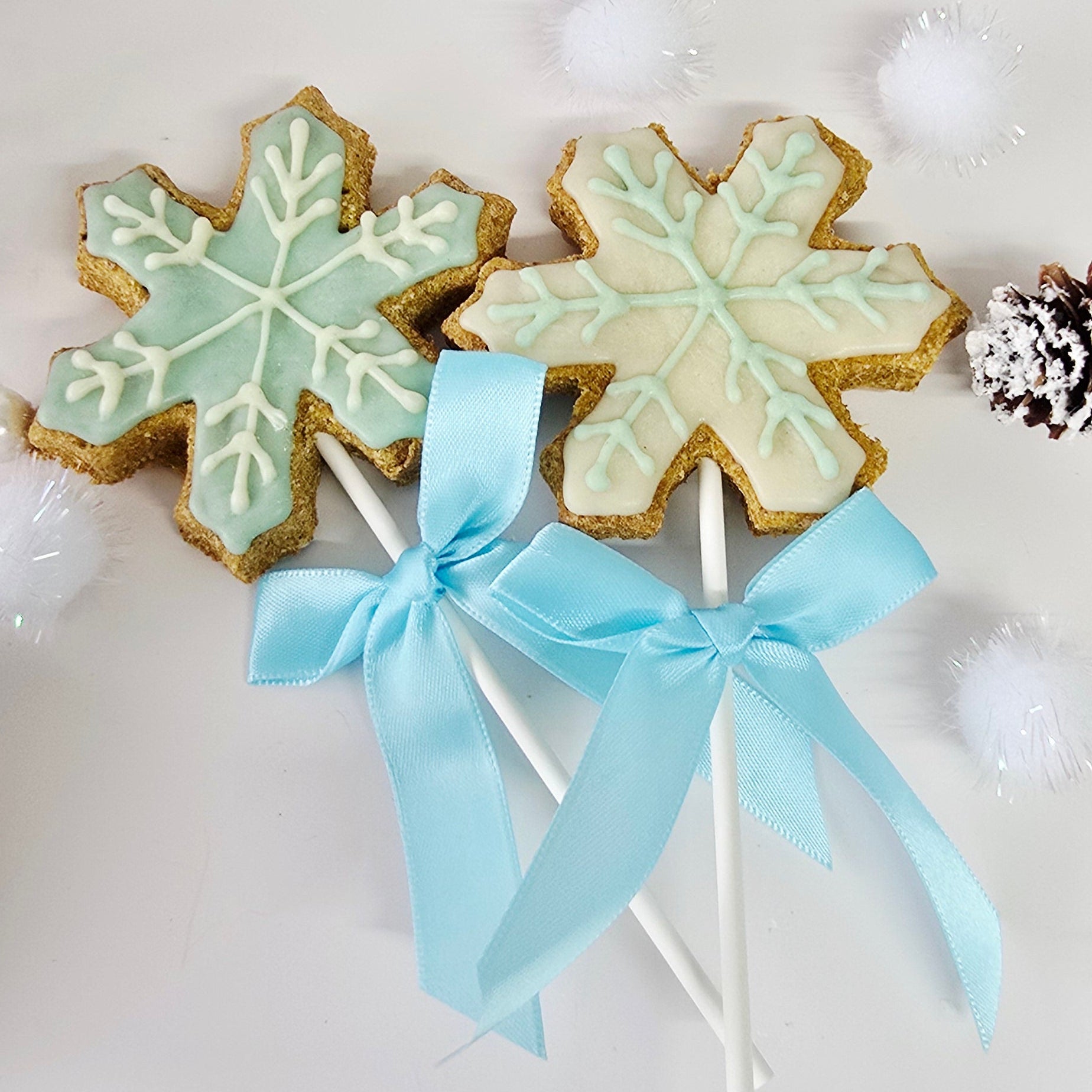 Decorative snowflake cookies on sticks with a blue ribbon against a snowy background.