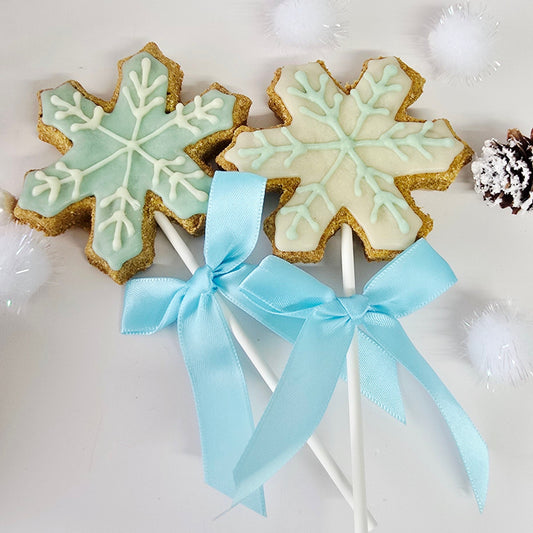 Decorative snowflake cookies on sticks with a blue ribbon against a snowy background.
