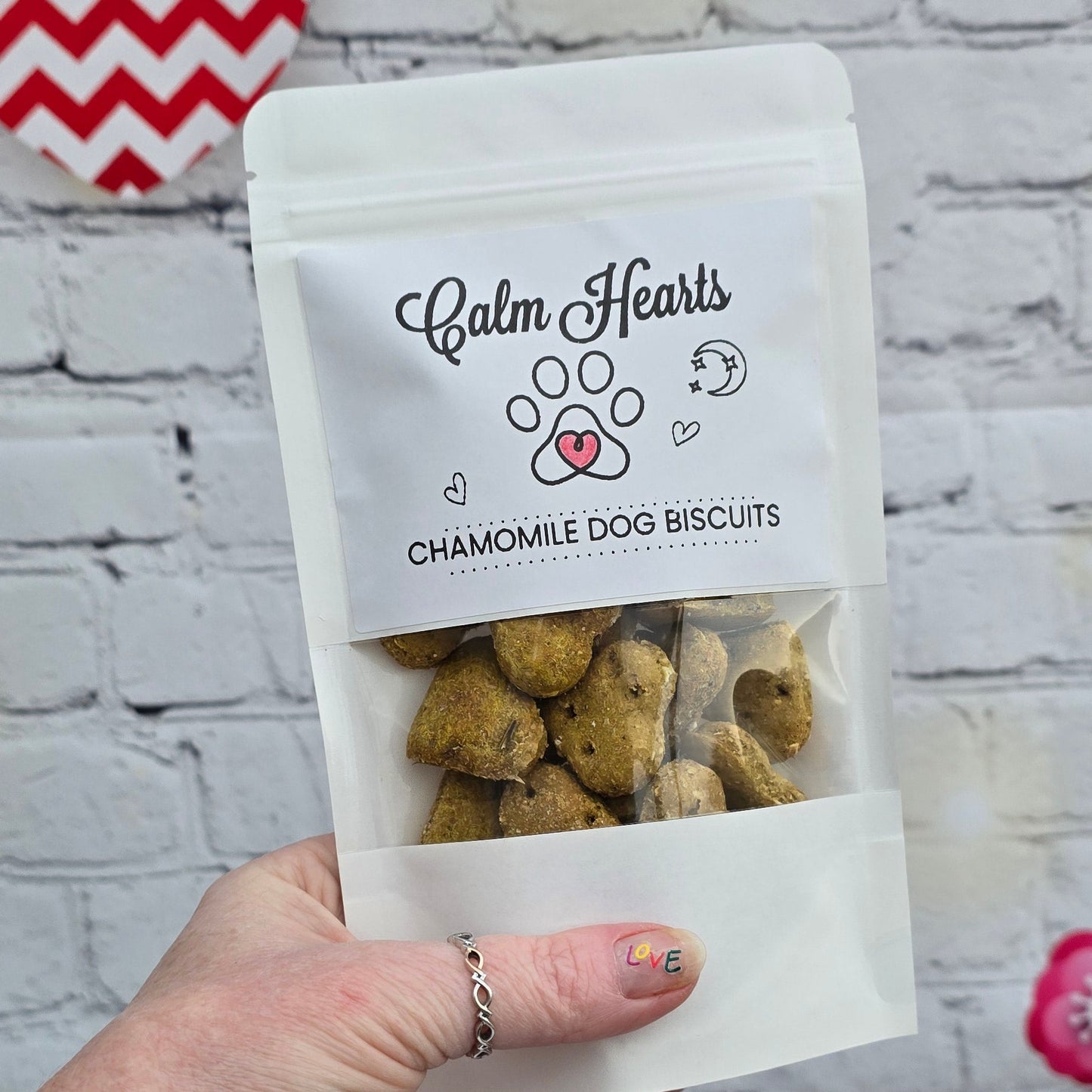 Hand holding a small bag of dog treats with a branded label on a textured surface.