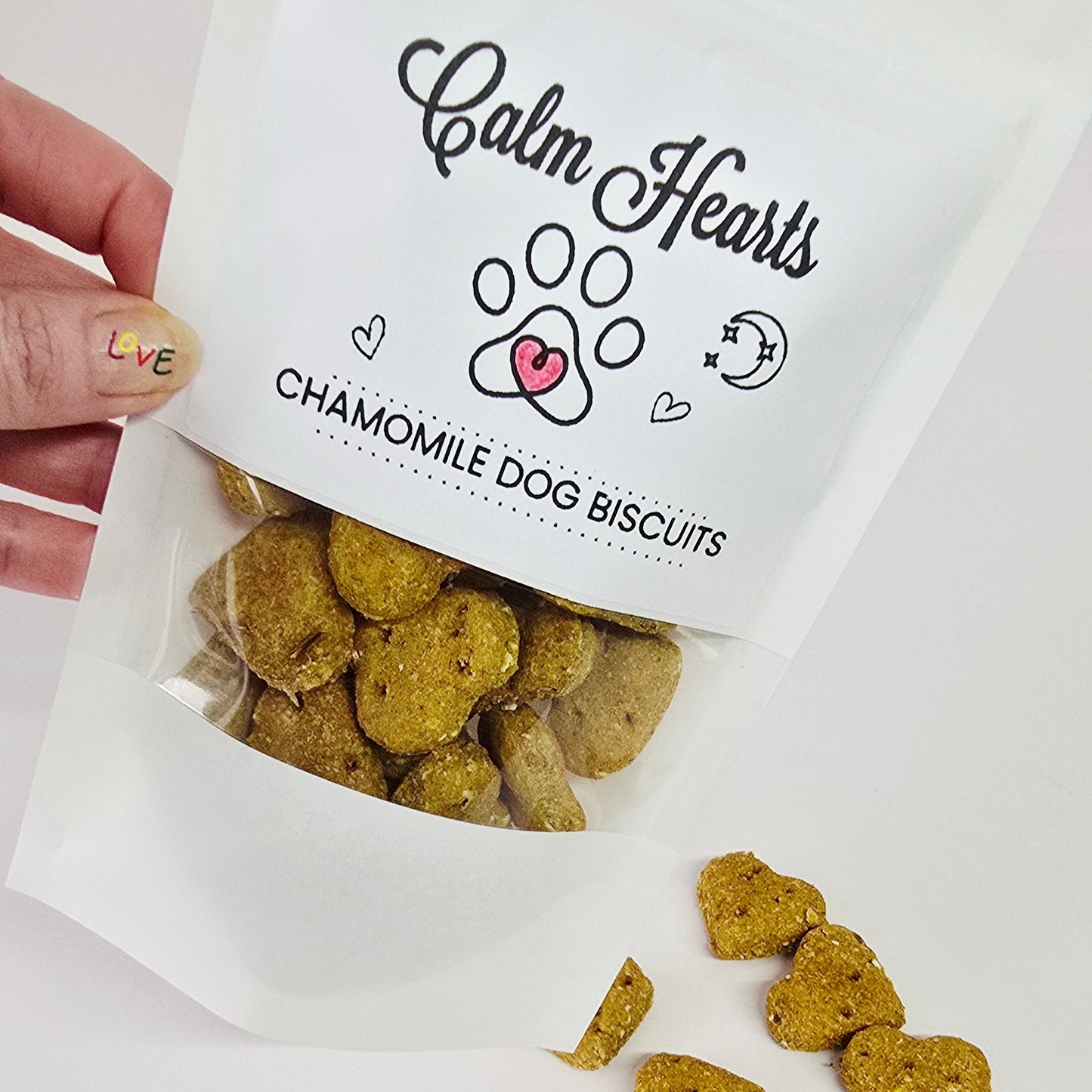 Bag of 'Calm Hearts' chamomile dog biscuits with a hand holding it on a white background.