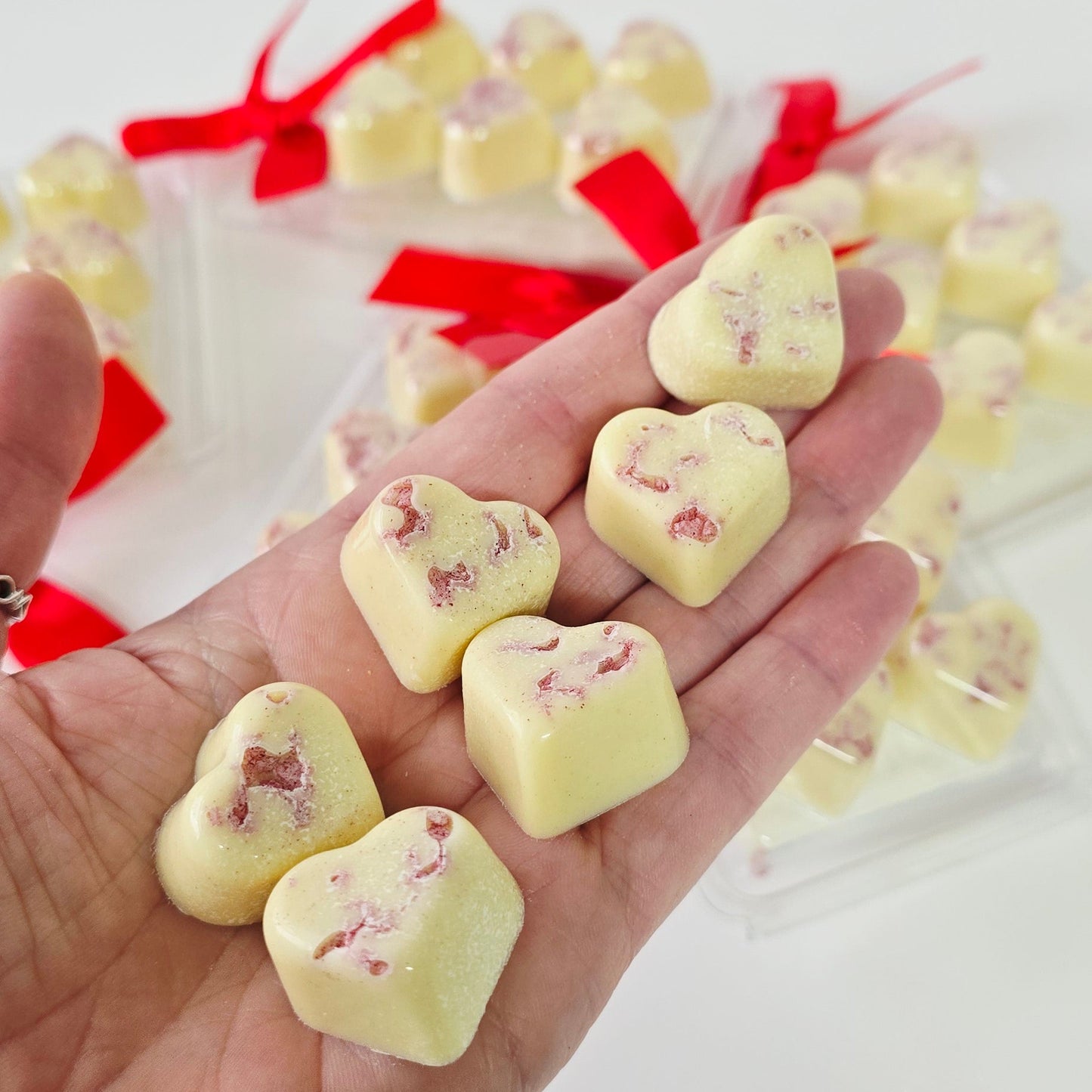 Hand holding heart-shaped white candies with red ribbons on a white background