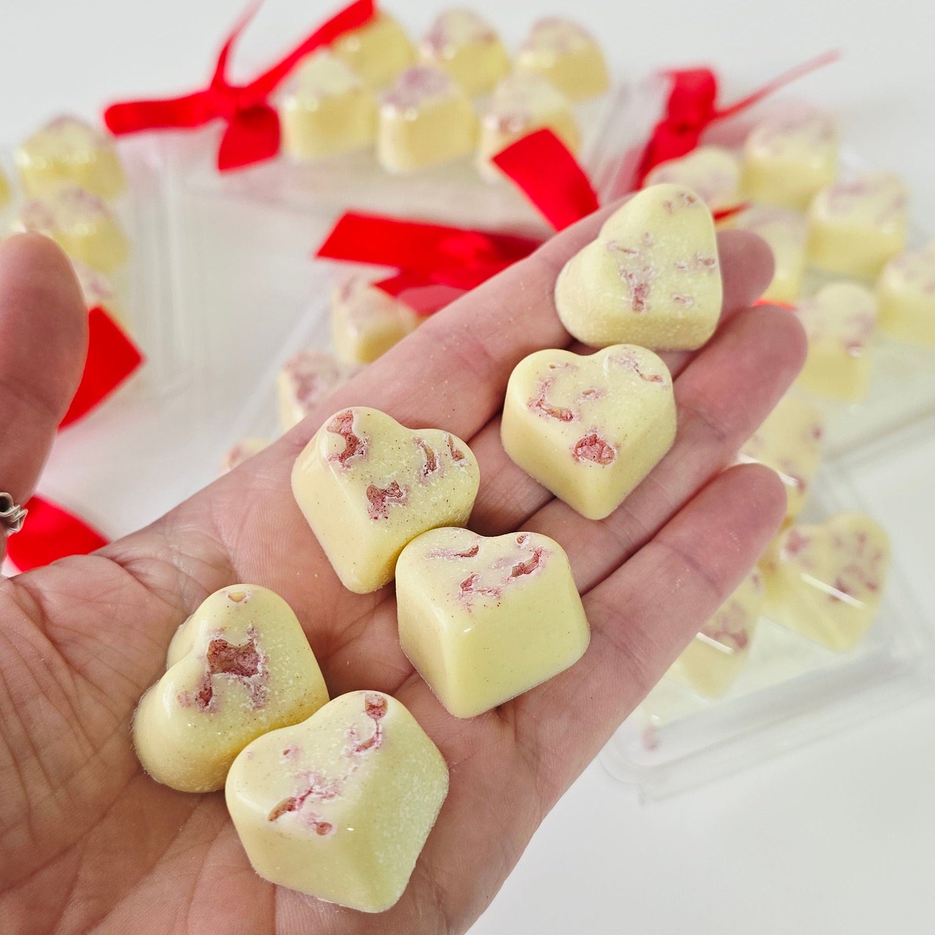 Hand holding heart-shaped white candies with red ribbons on a white background