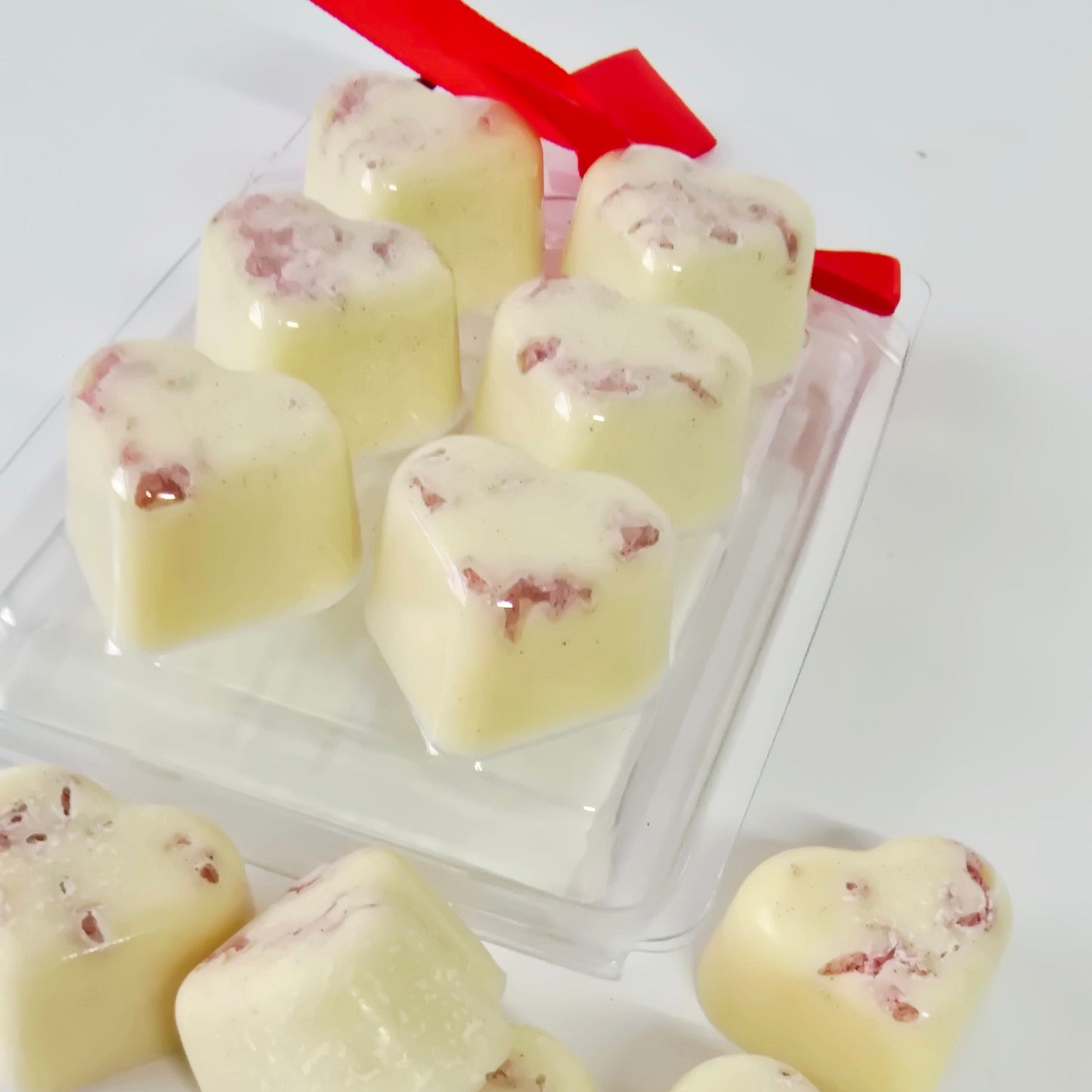 Heart-shaped white chocolate pieces with red berries on a white surface.