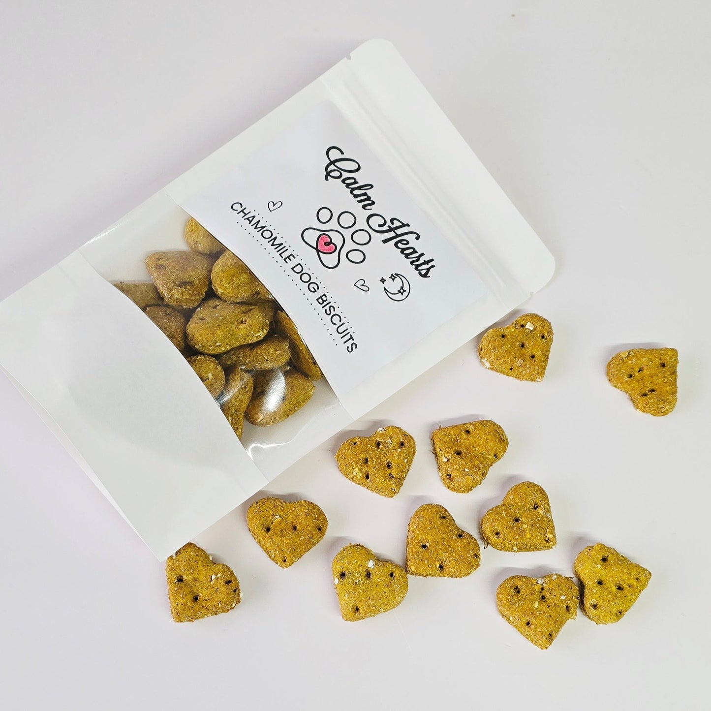 Heart-shaped dog biscuits spilling out of a white bag labeled 'Balm Hearts' on a light gray background.