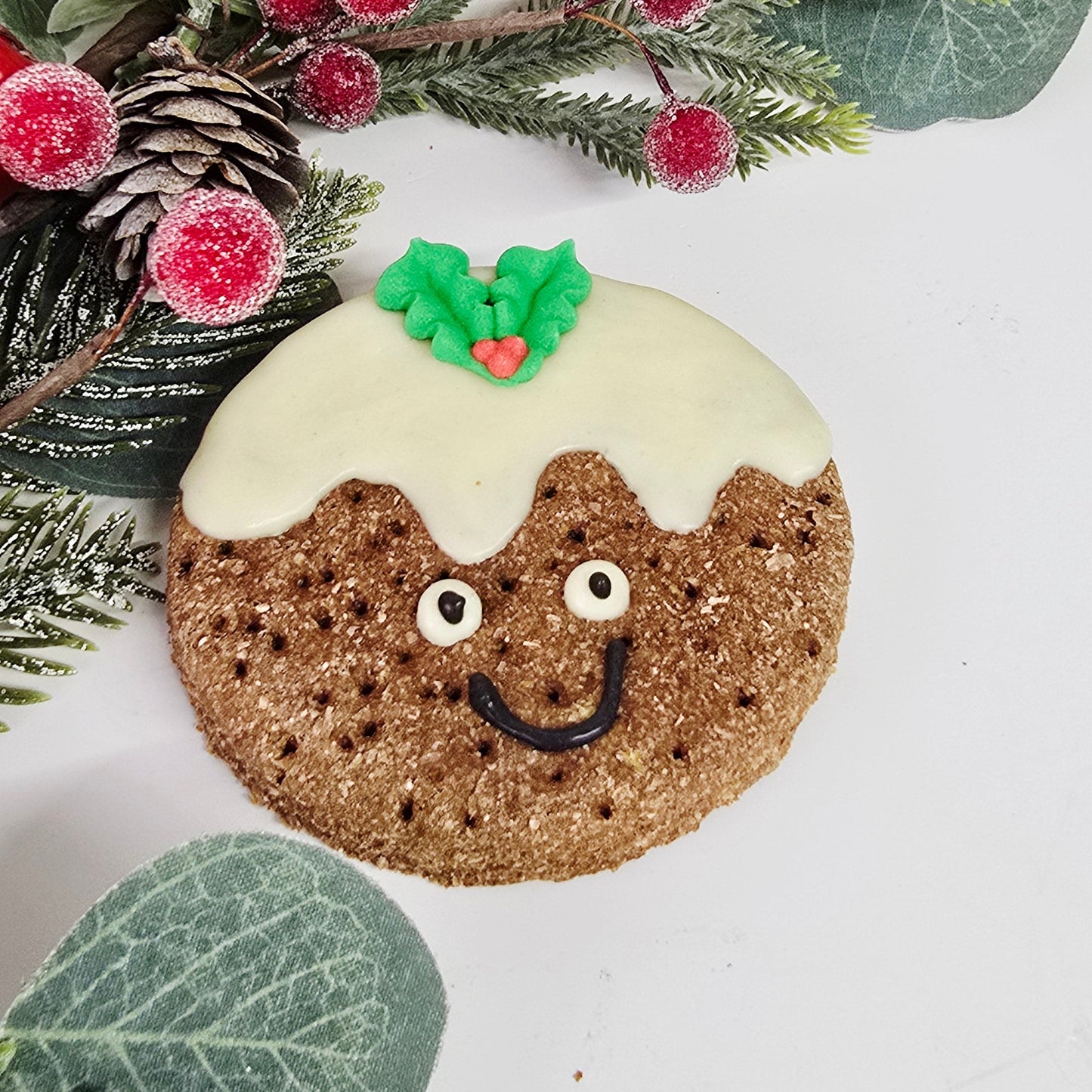 Decorative cookie shaped like a moon with a face, surrounded by greenery and berries on a white background