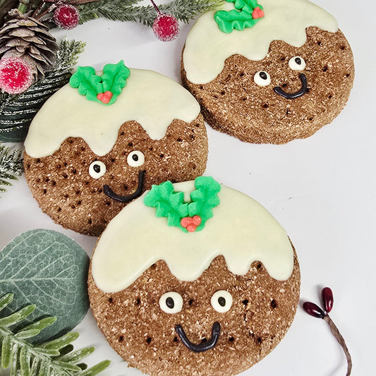 Decorative cookies shaped like Christmas trees with white frosting and green decorations, surrounded by festive foliage on a light background.